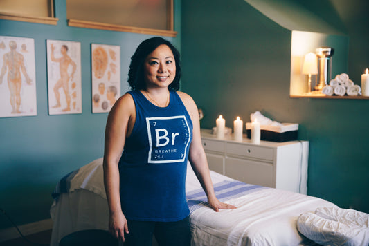 A massage therapist is in a serene blue room standing next to a massage table.