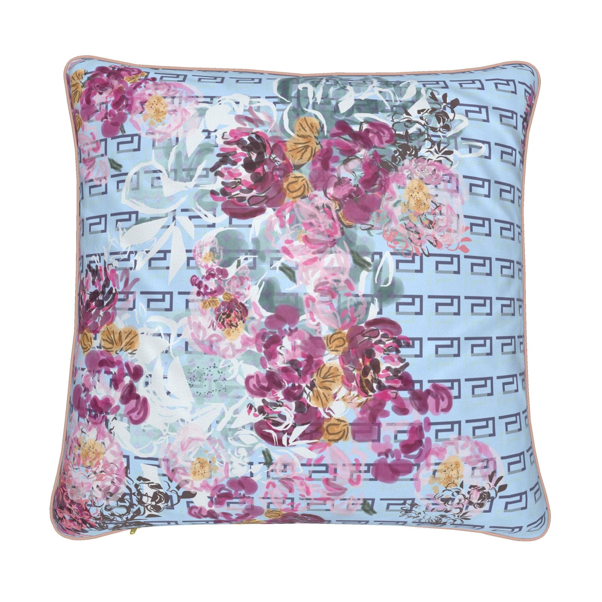 A square decorative throw pillow featuring a light blue background with a repeating dark gray Greek key pattern and a large watercolor-style floral print in pink, purple, and green, finished with a thin beige piped edge.