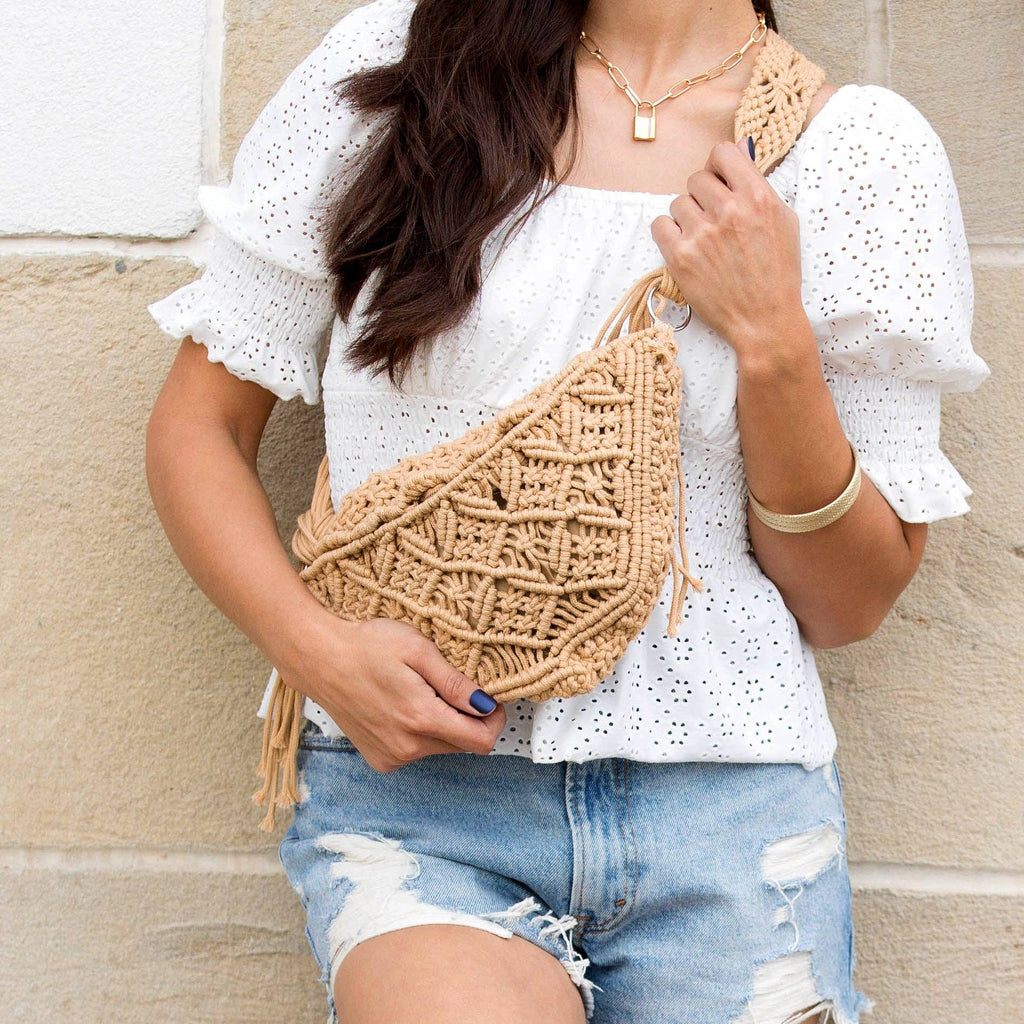 Person wearing a white blouse and denim shorts, holding a beige woven bag against a beige wall.