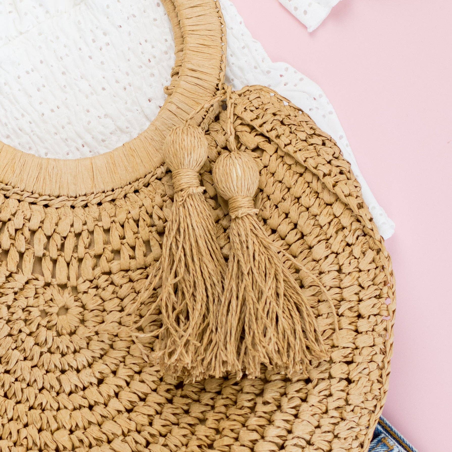 Beige woven bag with tassels on a white and pink background